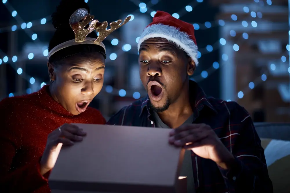 Couple surpris ouvrant un cadeau de Noël, serre-tête de renne et bonnet de Père Noël sur la tête