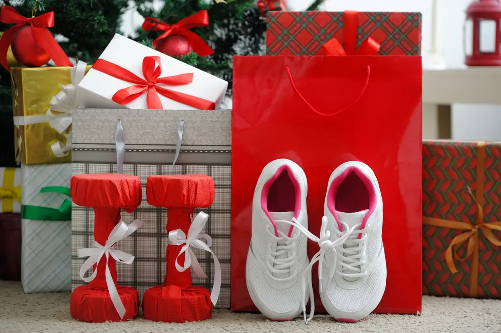 Haltères et baskets emballés de rubans au pied d’un sapin, idée de cadeau de Noël pour un passionné de sport