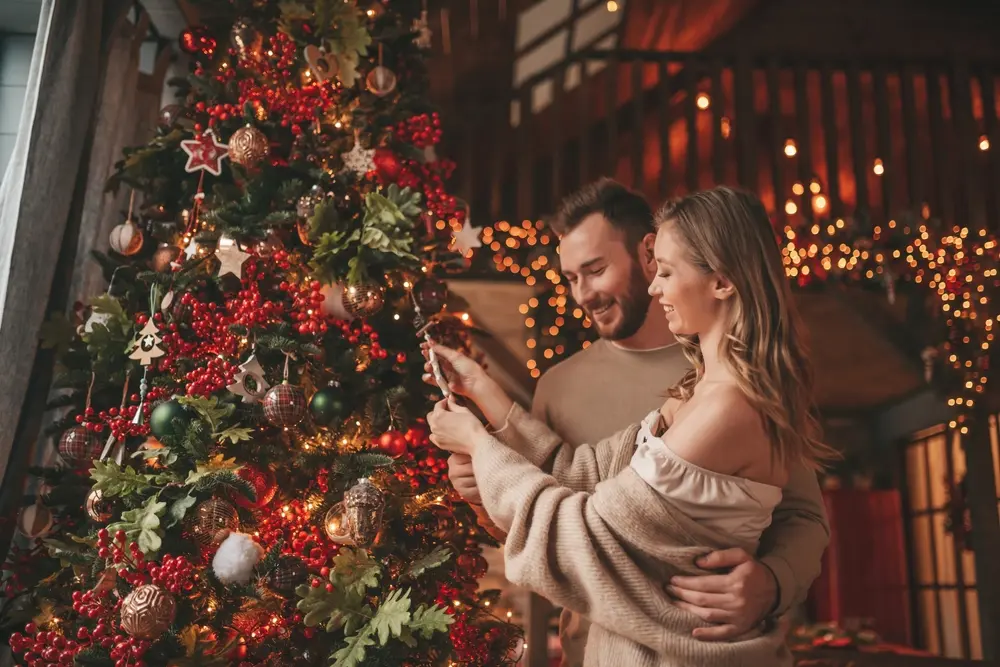 Couple souriant ouvrant ensemble un cadeau de Noël devant le sapin