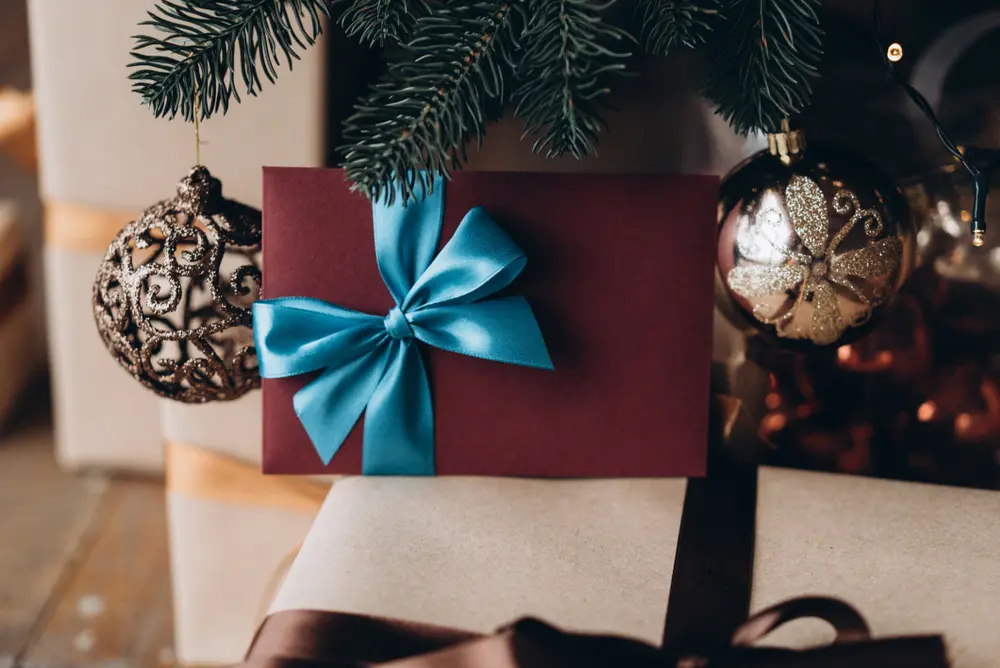 Enveloppe cadeau bordeaux nouée d'un ruban bleu, posée sous les branches d'un sapin de Noël