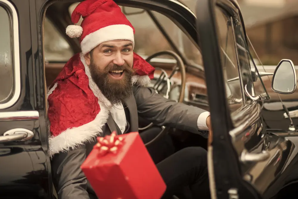 Homme en bonnet de Père Noël au volant d'une voiture ancienne, tendant un cadeau de Noël