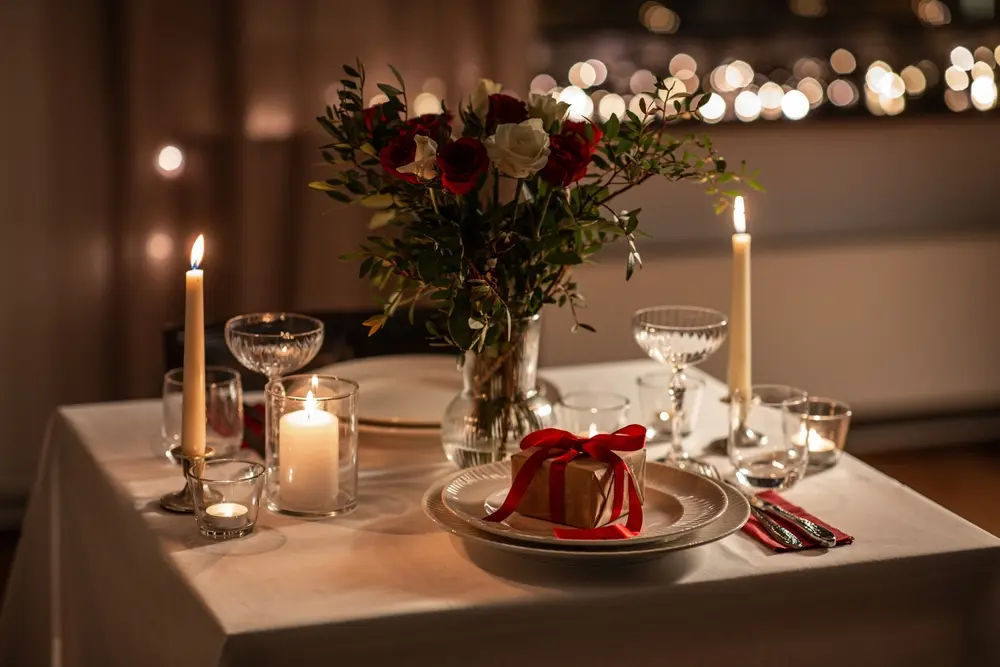 Table dressée pour deux aux chandelles, avec un bouquet de roses et un petit cadeau noué d'un ruban rouge posé sur une assiette