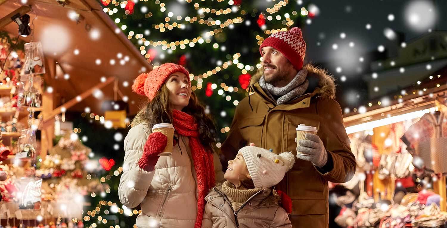 famiglia in un mercatino di natale con cioccolata calda in mano