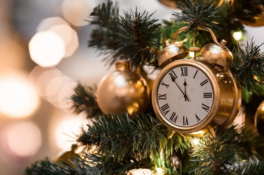 Réveil doré indiquant presque minuit, accroché dans un sapin de Noël à côté d’une boule dorée, pour un cadeau de dernière minute